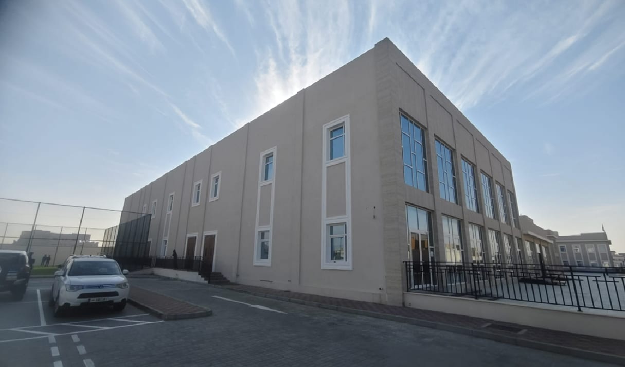 The completed two-storey school block, tall glazed bays at its corner above the car park